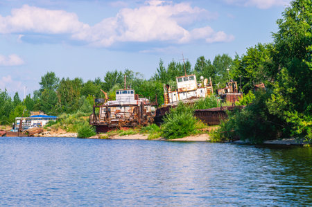 Old rusty ships lie on the river bank. The river bank and rusting ships. Pier with old ships on the shore. Old tugs are rusting on the riverbank.の写真素材