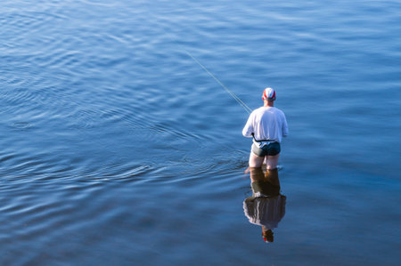A fisherman is fishing with a fishing rod in shallow water. Fishing on the river. In summer, relax on the river bank. A man goes fishing on the weekend.の写真素材
