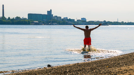 Swimming in the river in summer. A man is bathing in the river. Beach holidays on the water. A man in bright orange shorts is relaxing on the beach.の写真素材