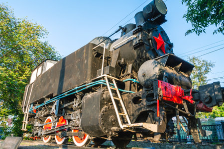 An old steam locomotive on a pedestal. History of railway locomotives. The locomotive is black with...