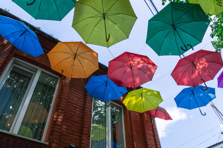 colorful streets. Colorful umbrellas suspended from above on the street near the houses. Decoration near houses made of umbrellas. Joyful atmosphere on the streets. Rainbow colors on umbrellas.の写真素材