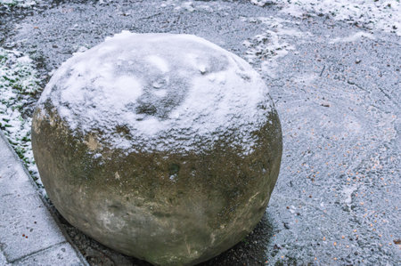 There is white snow on a large round stone. Natural stone of round shape without processing. Frosty weather in winter. Landscape design in the winter park. A stone lies against the background of snow.の写真素材