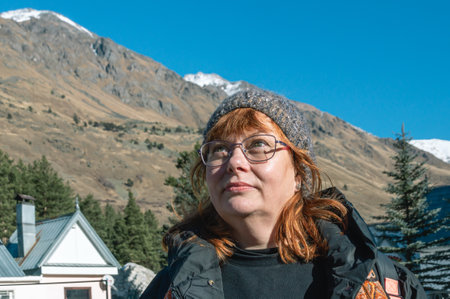A woman with red hair and a warm knitted hat at a ski resort. Rest in the mountains. A woman with...