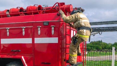 A firefighter in protective clothing descends from the roof of a fire truck. A fire truck and the work of a firefighter. A lifeguard at work. The rescue service.の写真素材