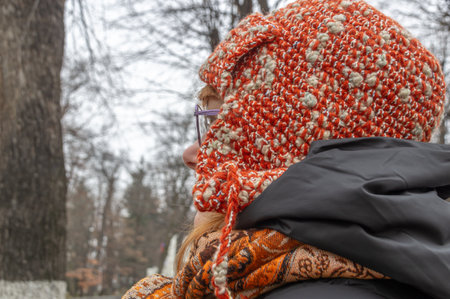 A red-haired woman in a knitted hat with ears and glasses. The woman looks ahead. A woman in a...