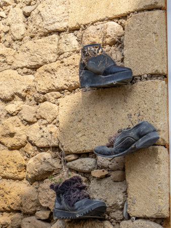 There are old shoes hanging on the wall of an old shell house. Old shoes on the background of the wall of an old limestone house.の写真素材