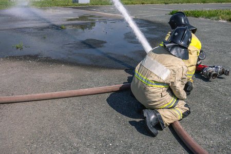 Firefighters in protective clothing hold the carriage fire barrel when supplying water to extinguish...
