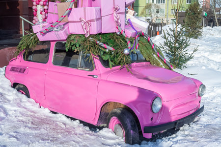 A pink subcompact in a snowdrift with New Year's gifts on the roof. A festive little car. A passenger car in the snow with Christmas gifts.の写真素材