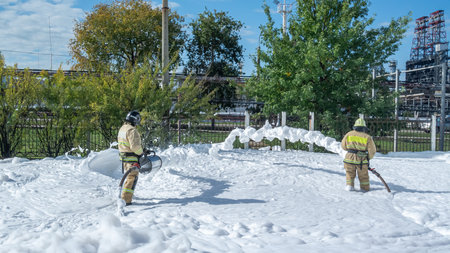 Firefighters in protective clothing use a foam generator to supply foam to extinguish the fire. Fire extinguishing foam spreads over a large area. The rescue service. Firefighters extinguish the fire.の写真素材