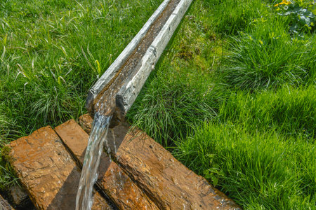 Pure spring water flows through a wooden chute carved from wood. Environmentally friendly artesian water. A traditional antique pipeline. A stream of water flows through a chute in the village.の写真素材
