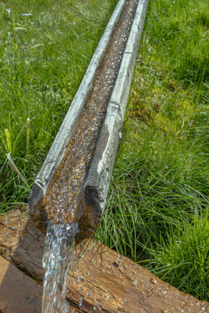 Pure spring water flows through a wooden chute carved from wood. Environmentally friendly artesian water. A traditional antique pipeline. A stream of water flows through a chute in the village.の写真素材