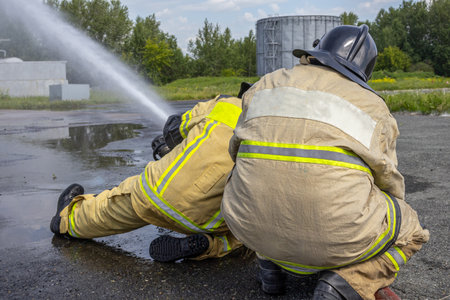 It is very difficult for firefighters to hold a fire barrel when water is supplied under high pressure. Firefighters extinguish a fire at an oil refinery. Firefighters' uniforms.の写真素材