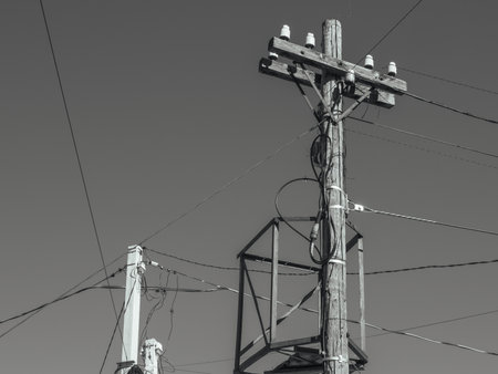 The old wooden pole of the power transmission line providing electricity to residential buildings is in need of repair.A concrete power line support is visible behind a wooden pole with electric wiresの写真素材