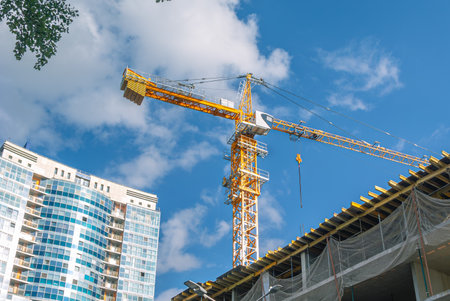 A tower construction crane on the background of a blue sky with clouds. The frame of a building under construction. Building construction. Load-bearing reinforced concrete walls of the house.の写真素材