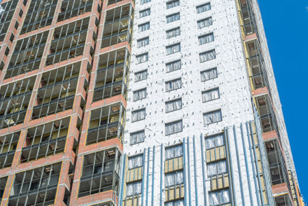 Construction work on the exterior cladding. Laying waterproofing material on the walls of a high-rise building. Insulation of the house. Balconies of a house under construction.の写真素材