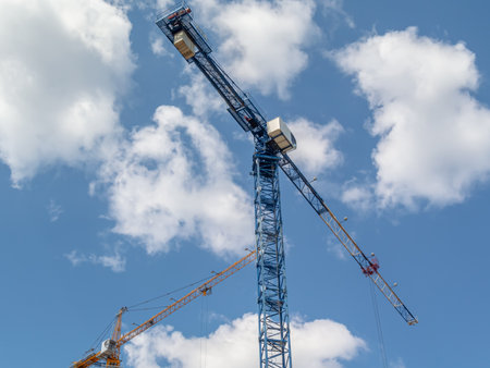 A large number of tower construction cranes are involved in the construction of a new residential area. Construction equipment. Tower cranes among the trees and the blue sky with clouds.の写真素材