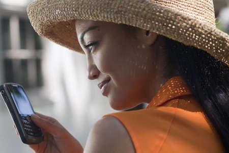 Close-up side view of a young woman wearing a sun hat and texting on her cell phone. Horizontal format.の写真素材