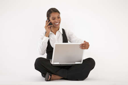 Young woman sitting on floor using laptop and cell phone. Horizontally format.の写真素材