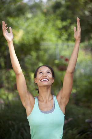Young woman with arms raised in outdoor setting. Vertically framed shot.