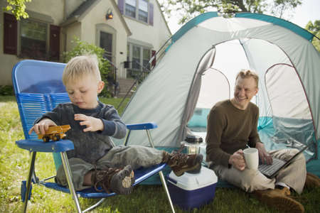 Father with laptop and son playing while camping in the front yardの写真素材
