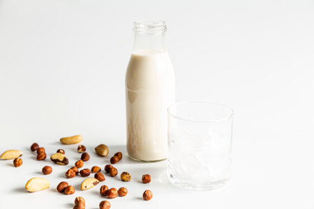 Almond milk in a glass bottle with nuts on a white backgroundの写真素材