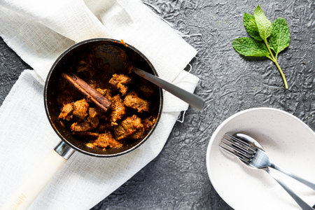 Pork in red curry paste in pan on stone table background, top view
