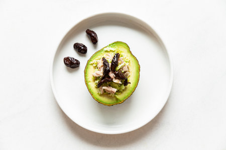Stuffed avocado with dried dates on a white plate on a white background