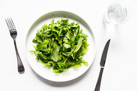 Fresh green salad with arugula, arugula leaves and cutlery on white background