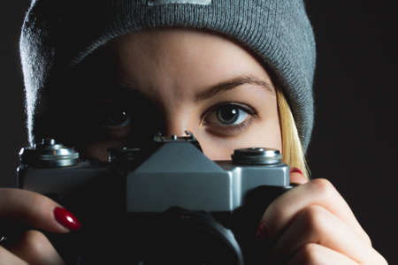 closeup of hipster girl eyes taking picture with retro camera wearing winter hat on dark backgroundの写真素材