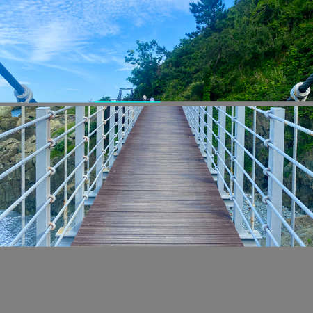 A vertical shot of a wooden bridge leading to the sea under a blue skyの写真素材
