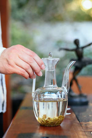 A woman's hand pours tea from a decanter into a glass jar.の写真素材