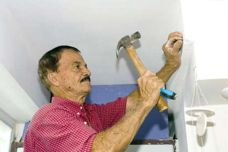 A senior man hammers nail into wall.  He is of Puerto Rican ethnicity.の写真素材