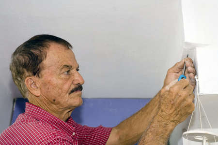 A senior man uses a screwdriver to screw in a small screw into a wall.の写真素材