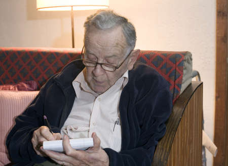 A senior man sits and writes on a pad.の写真素材