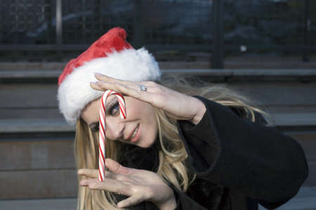 A Caucasian woman holding a candy cane and wearing a Santa hat.の写真素材
