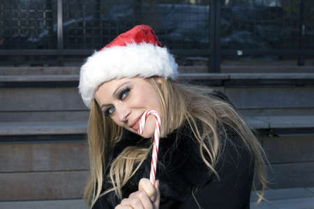 A Caucasian woman holding a candy cane and wearing a Santa hat.の写真素材