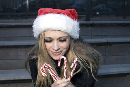 A Caucasian woman holding candy canes and wearing a Santa hat.の写真素材