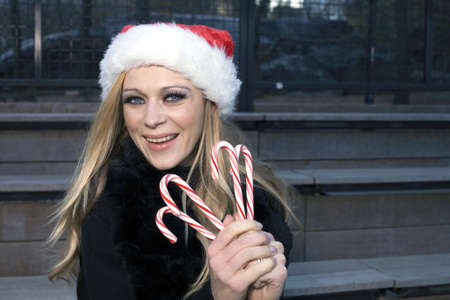 A Caucasian woman holding candy canes and wearing a Santa hat.の写真素材