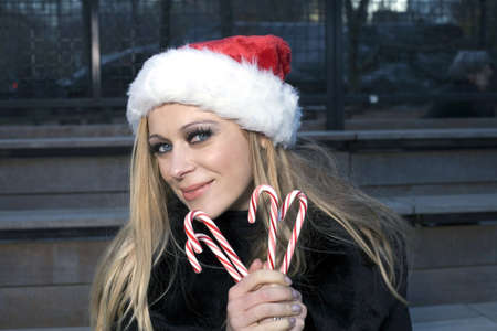 A Caucasian woman holding candy canes and wearing a Santa hat.の写真素材