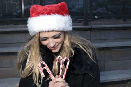 A Caucasian woman holding candy canes and wearing a Santa hat.の写真素材
