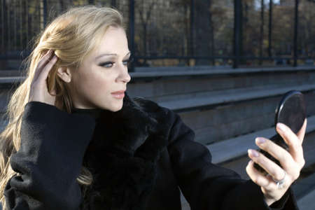 A Caucasian woman adjusts her hair while looking in mirror.の写真素材