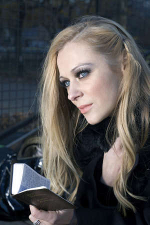 Caucasian woman holding a small Bible while outdoors 