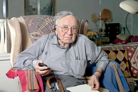 A senior man sits on his couch with his headphone device.  の写真素材