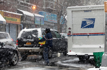 BRONX, NEW YORK -JANUARY 7:  Mailman carries package for delivery during snow storm.  Taken January 7, 2017 in New York.のeditorial素材