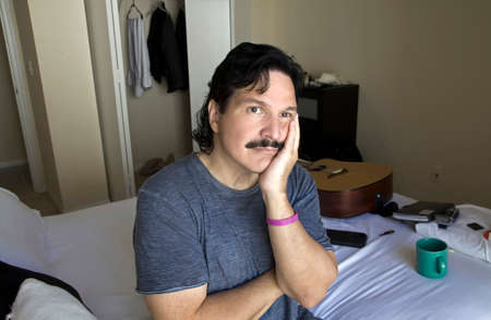 Hispanic man with bored or sad look on his face while sitting on his bed.の写真素材