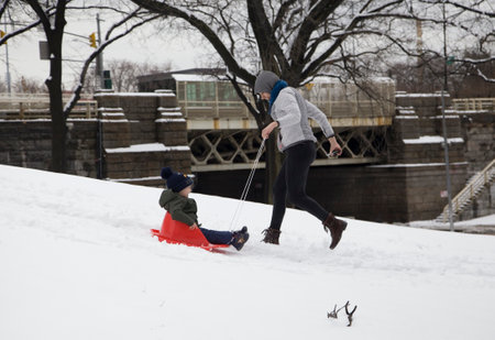BRONX, NEW YORK/USA - March 2, 2019: A mother helps her child ride a sleigh in snow at park near Yankee Stadium.のeditorial素材