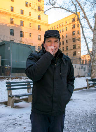 Hispanic man warming hand with breath while outdoors in winter.