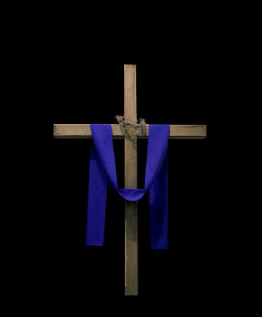 Wood cross draped with purple fabric and thorns isolated against black background.の写真素材