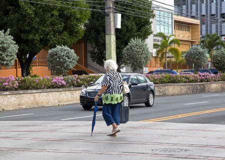 BAYAMON/PUERTO RICO - February 26, 2019: Elderly woman crosses street with umbrella.のeditorial素材