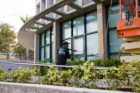 BAYAMON/PUERTO RICO - February 26, 2019: Hispanic man uses high pressure washer machine to clean exterior of building glass.のeditorial素材